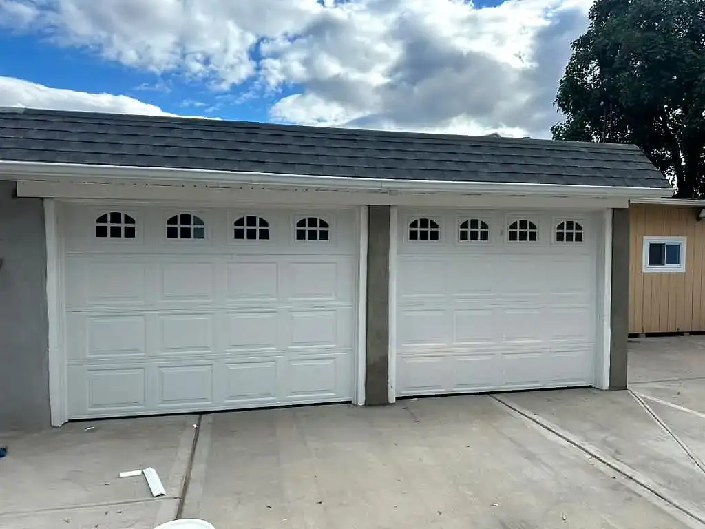 Two white carriage doors with arched windows on a new build