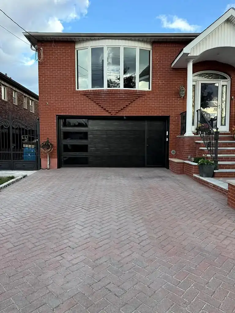 Black flush door on a red-brick home with a paver driveway